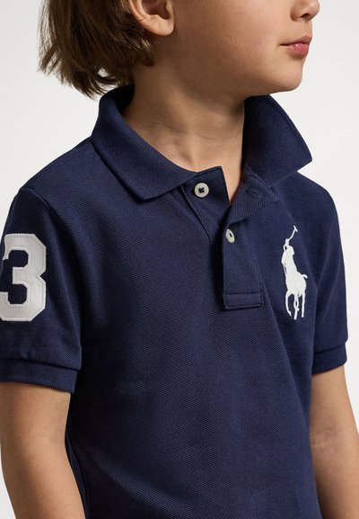Námornícky modré polo tričko s textúrovanou tkaninou, obsahujúce biele vyšívané logo a bielu číslicu „3“ na ľavom rukáve.