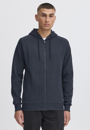 Navy zip-up hoodie with a hood, featuring a textured fabric, ribbed cuffs, front pockets, and contrasting diagonal panel detailing.