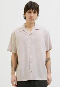 Chemise rose clair à manches courtes avec un col à revers, fermeture à boutons et texture lisse. Présente un léger éclat du tissu et un ourlet arrondi.