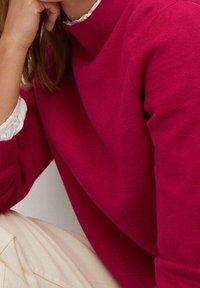 Fuchsia Pullover mit hohem Kragen und langen Ärmeln, kombiniert mit einem weißen Rüschenshirt. Weiche Textur und figurbetontes Design.