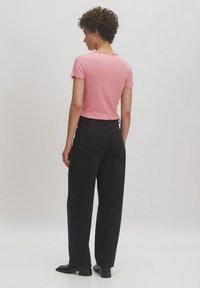 Roze geribde top met korte mouwen en ruches aan de rand, gecombineerd met hoge zwarte broeken en zwarte schoenen. Minimalistisch ontwerp, casual pasvorm.