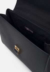 Sac à main noir avec un extérieur texturé, featuring un fermoir en métal doré et un intérieur spacieux, étiqueté "ANNA FIELD."