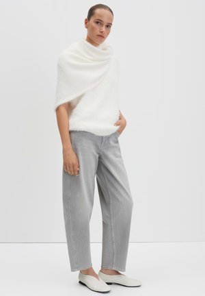 Witte, fuzzy brei oversized trui gecombineerd met lichtgrijze wijde broek en crèmekleurige instappers, geplaatst tegen een simpele witte achtergrond.