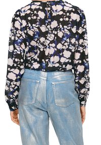 Schwarzbluse mit floralem Muster und puffigen Ärmeln, kombiniert mit hellblauen metallischen Jeans mit Gesäßtaschen und tailliertem Schnitt.