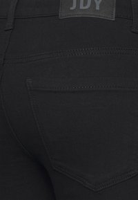 Calças de ganga pretas com uma textura lisa, dois bolsos traseiros com costura discreta e uma etiqueta de pele com a marca acima da cintura.