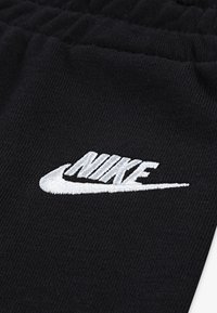 Črne jogger hlače iz blaga z elastiko v pasu, ki imajo na strani belo vezeno Nike logo. Mehak material, minimalističen dizajn.