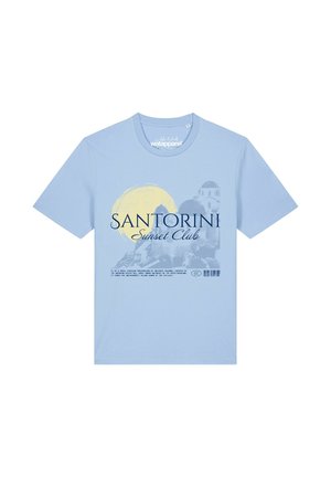 T-shirt bleu clair avec un graphisme du coucher de soleil à Santorin, soleil jaune et bâtiments blancs, avec le texte "Santorini Sunset Club" et un petit texte descriptif en dessous.