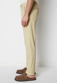 Beige, straight-leg trousers with a smooth texture and side pockets. Worn with brown slip-on shoes for a casual look.