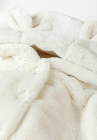 Mehakava bijela umjetna krzna jakna s kapuljačom, s velikim gumbima i teksturiranim materijalom. Dizajn ima udoban, plišan izgled i glatku unutrašnjost.