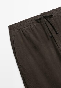 Brune corduroy bukser har et snoreliv og to sidelommer, med lodret ribbet tekstur og en afslappet pasform.