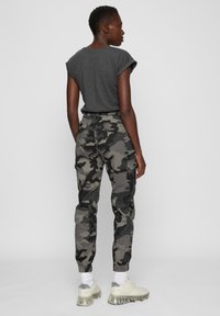 Pilka marškinėliai su sukimtais rankogaliais, derinami su kamufliažinėmis kargo kelnėmis. Kelnėse yra kišenės, siauras kirpimas ir elastingi rankogaliai. Kasdieniai balti sportbačiai.