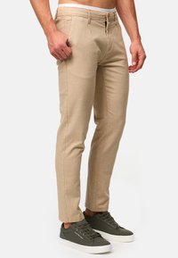 Beige chinos med en figursydd design, laget av teksturert stoff. Har sidelommer og belte med knapp, kombinert med mørke sneakers.