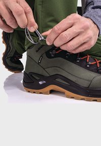 Grüner Wanderschuh mit schwarzen Akzenten und orangefarbenen Schnürsenkeln. Verfügt über strukturiertes Leder und eine strapazierfähige Gummisohle mit tiefen Profilen für besseren Halt.