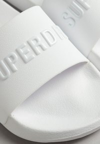 Sandalias de playa blancas hechas de material sintético texturizado. Cuentan con una correa ancha con el logotipo en relieve "SUPERDRY". Suela interior suave.