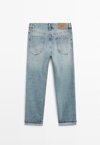 Lichtblauwe spijkerbroek met opgerolde pijpen, twee achterzakken, riemlussen en een bruin leren merklabel op de tailleband.