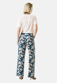 Weite Hosen aus türkisfarbenem Stoff mit einem floralen und paisleymuster in Weiß und Pink. Kombiniert mit einem leichten, texturierten Kurzarmoberteil.
