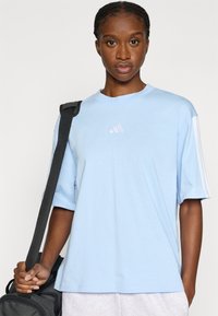 Ανοιχτό μπλε βαμβακερό T-shirt με κοντά μανίκια, που φέρει ένα μικρό λευκό λογότυπο στο στήθος και λευκές ρίγες κατά μήκος των μανικιών.