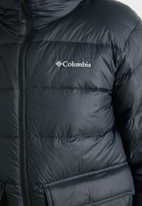 Marineblå Columbia dunjakke med glidelås, quiltet tekstur og logo. Inkluderer to sidelommer og design med høy krage.
