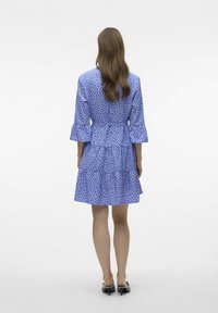 Niebieska sukienka w biały kwiatowy wzór, z rękawami 3/4, falbanowym dołem, wcięciem w talii i rozkloszowanym krojem. Gładka faktura materiału.