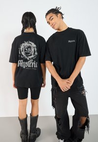 Black graphic t-shirt featuring a rose design on the back and "Mysteria" text; paired with black ripped jeans and knee-high boots.
