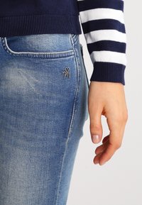 Marinblå och vit randig tröja med ribbad nederkant som är kombinerad med ljusblå jeans med en liten hjärtdekor på bakfickan.