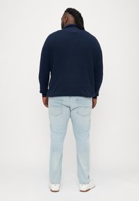 Σκούρο μπλε πλεκτό πουλόβερ με ψηλό γιακά, συνδυασμένο με ανοιχτό μπλε τζιν. Λευκά αθλητικά παπούτσια ολοκληρώνουν την εμφάνιση, με διακριτές λεπτομέρειες στην πίσω τσέπη.