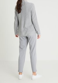 Grauer Rippstrickpullover mit abgerundetem Saum, kombiniert mit passenden grauen, schmal geschnittenen Jogginghosen. Der glatte Stoff und die weißen Sneaker runden das Outfit ab.