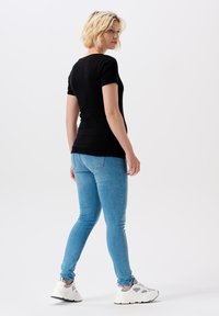 Sort kortærmet T-shirt, tætsiddende design. Parret med lyseblå jeans og hvide sneakers. Glat tekstur, minimalistisk stil.