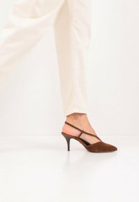 Chaussure slingback en daim marron avec un bout pointu, une fine bride à la cheville et un talon aiguille bas et texturé, posée sur un fond clair.