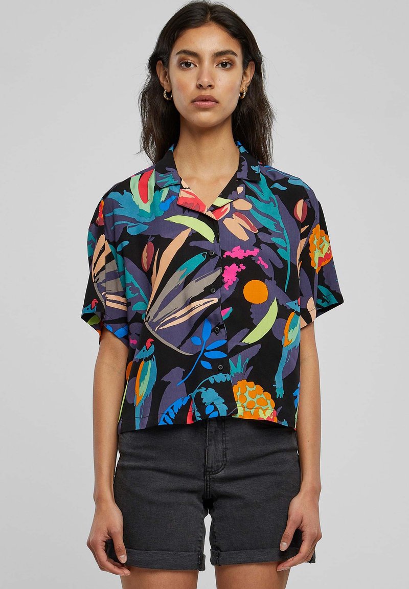 Blusa nera a maniche corte con un vivace motivo floreale in vari colori. Tessuto leggero, vestibilità ampia e chiusura a bottoni nella parte anteriore.