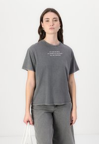 Gray cotton t-shirt with short sleeves, round neckline, and text printed in white, paired with matching gray pants. Smooth texture, relaxed fit.