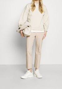 Beige oversized sweatshirt med puffärmar, beige slim-fit byxor och vita sportskor. Bär en strukturerad beige handväska.