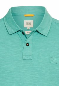Türkises Polohemd aus Bio-Baumwolle mit kurzen Ärmeln, Knopfleiste am Kragen und einem kleinen Logo-Label auf der linken Brust.