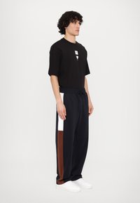Sort kortærmet t-shirt med grafik og afslappede navy sweatpants med hvide og brune sidelæg, suppleret af hvide sneakers.