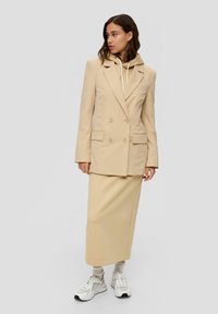 Beige pinstripe kaksirivinen bleiseri, yhdistettynä samansävyiseen neulehameeseen, valkoisen hupparin ja valkoisten tennareiden päällä.