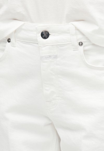 Λευκό τζιν παντελόνι με ορατό κουμπί και ελάσματα, με το "CLOSED" χαραγμένο στο μεταλλικό κουμπί και στην υφασμάτινη ετικέτα.