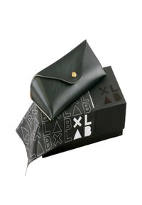 Svart läderfodral med en vikbar klaff och mässingsknapp, vilande på en svart låda med monokroma geometriska mönster och logotyp.