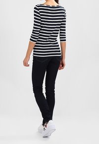 Granatowo-biały top w paski z długim rękawem i okrągłym dekoltem, zestawiony z ciemnymi dżinsami i białymi trampkami z czerwonym akcentem w kształcie gwiazdy.