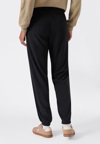 Zwarte sweatpants met een elastische tailleband, taps toelopende pijpen en boorden bij de enkels, gecombineerd met lichtbruine sneakers en witte sokken.