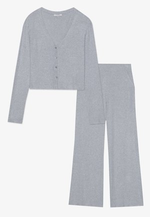 Hellgraues geripptes Strickset mit einer verkürzten Strickjacke mit Knopfverschluss und langen Ärmeln, kombiniert mit weit geschnittenen Hosen mit Taschen.