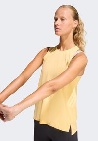 Top deportivo sin mangas de color amarillo claro con un ajuste relajado, que presenta discretas aberturas laterales y detalles de marca en un diseño contrastante.