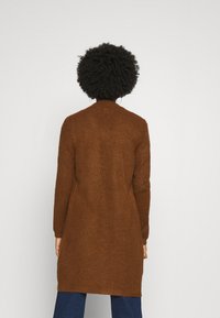 Brązowy sweter kardigan o długiej sylwetce, żebrowanej fakturze i długich rękawach. Standardowy kołnierz i boczne rozcięcia zapewniające swobodę ruchów.