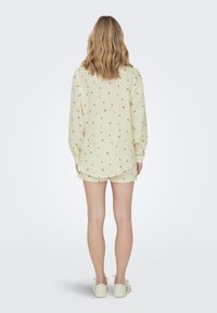 Ensemble composé d'une chemise à manches longues jaune clair et d'un short avec de petits motifs floraux rouges, fabriqué en tissu doux. Coupe décontractée avec un ourlet légèrement arrondi.