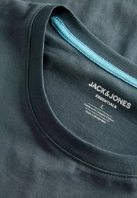 Σκούρο γκρι T-shirt με στρογγυλή λαιμόκοψη. Διαθέτει εσωτερικό περιθώριο γύρω από τη λαιμόκοψη σε ανοιχτό μπλε χρώμα, ετικέτα με το λογότυπο της μάρκας και οδηγίες φροντίδας. Κατασκευασμένη από οργανικό βαμβάκι.