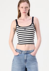 Černobílé pruhované žebrované cropped top s širokými ramínky a malým logem. V kombinaci se světlými modrými džíny s vysokým pasem a uvolněným střihem.