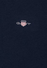T-shirt in cotone blu navy con un piccolo logo GANT che presenta un design a scudo, con strisce rosse e bianche e tre stelle.