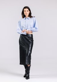 Lichtblauw oversized button-up shirt met lange mouwen, gecombineerd met een zwarte leren midi-jurk en zwarte puntige cowboylaarzen.