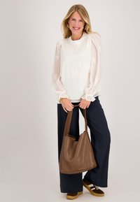 Witte blouse met doorschijnende pofmouwen, bloemige borduursels; gecombineerd met marineblauwe broek en een bruin leren schoudertas; bruine platform sneakers.