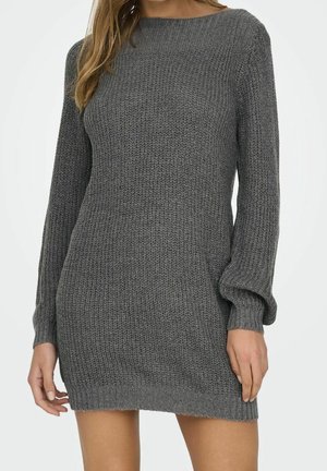 Kobieta ubrana w długi sweterkowy szary sweter z dzianiny z fakturowanym wzorem oraz ściągaczami na rękawach i dole.