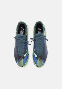 Scarpe sportive con un motivo geometrico blu e verde, superficie testurizzata e suola in gomma nera, dotate di lacci e logo iconico.